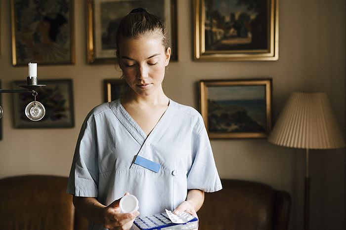 Kvinna i arbetskläder tittar på en medicindosett