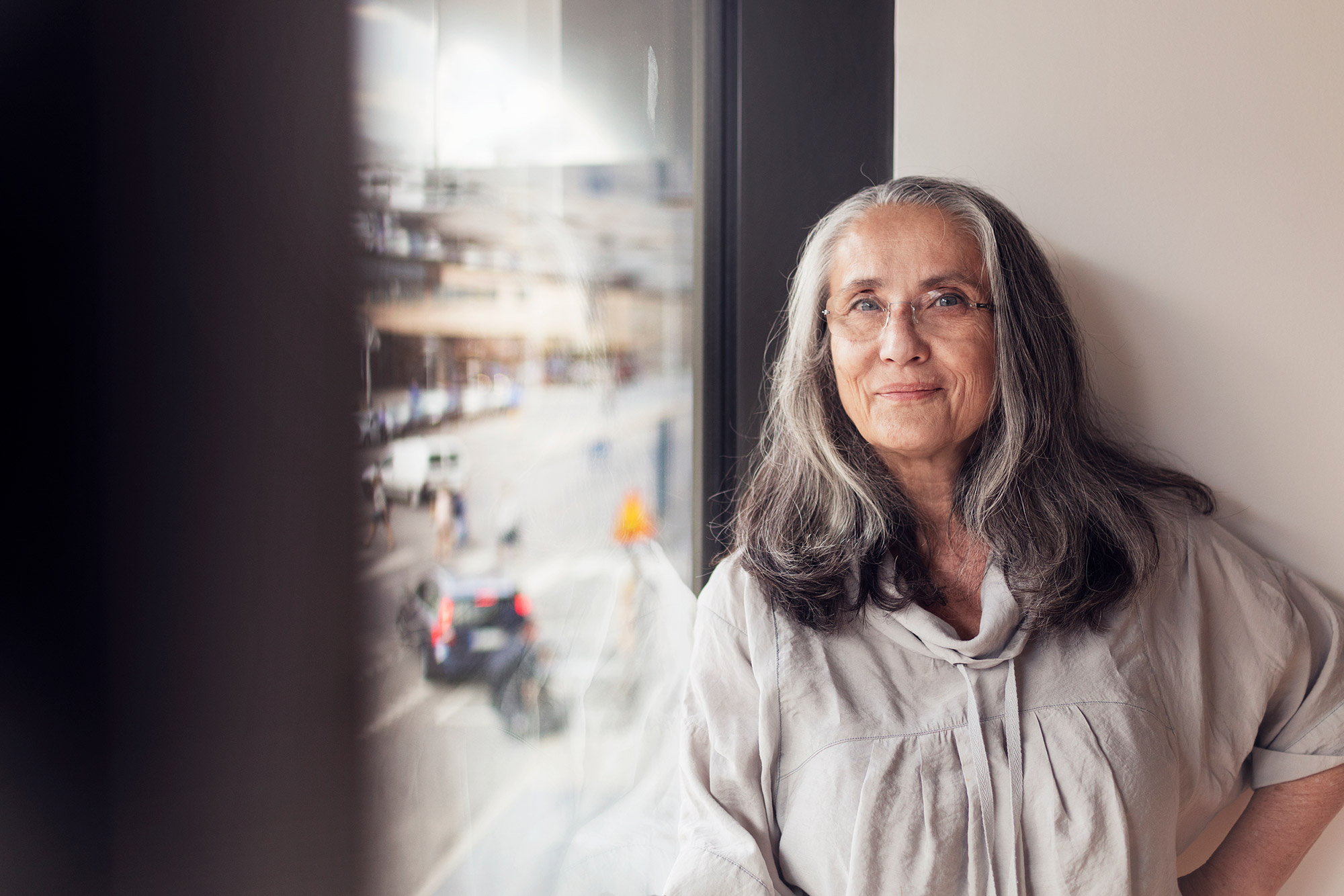 Leende kvinna med långt grått hår står vid fönster