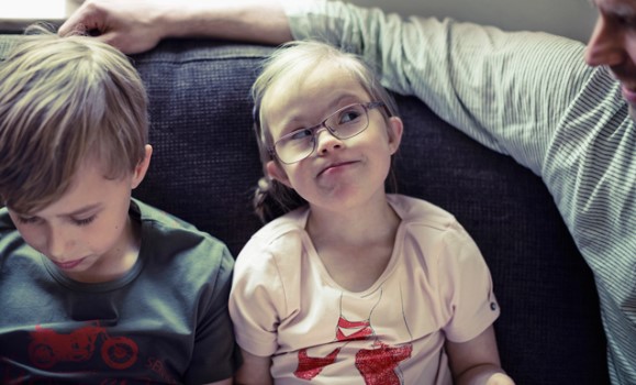 Två barn med funktionsnedsättning sitter i en soffa