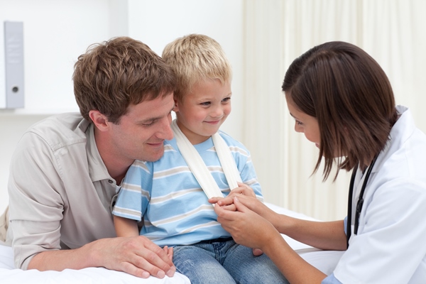 Patient hos läkare på vårdcentral Liten pojke sitter i sin faras knä och undersöks av vårdpersonal.
