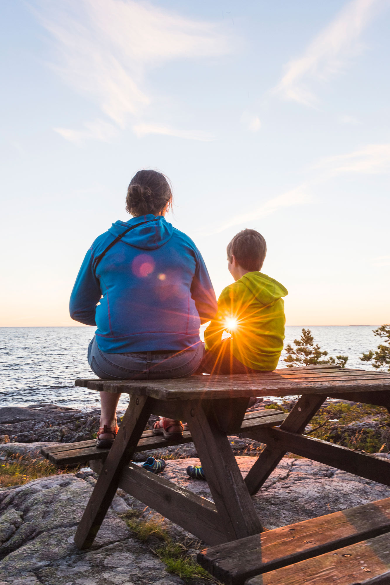 En vuxen och ett barn sitter på en bänk med ryggen mot kameran