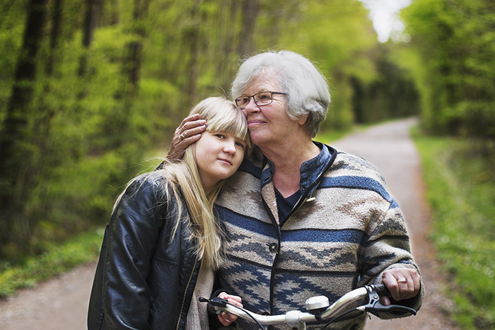 Äldre kvinna armen om en yngre kvinna. De står vid en cykel ute i naturen. 