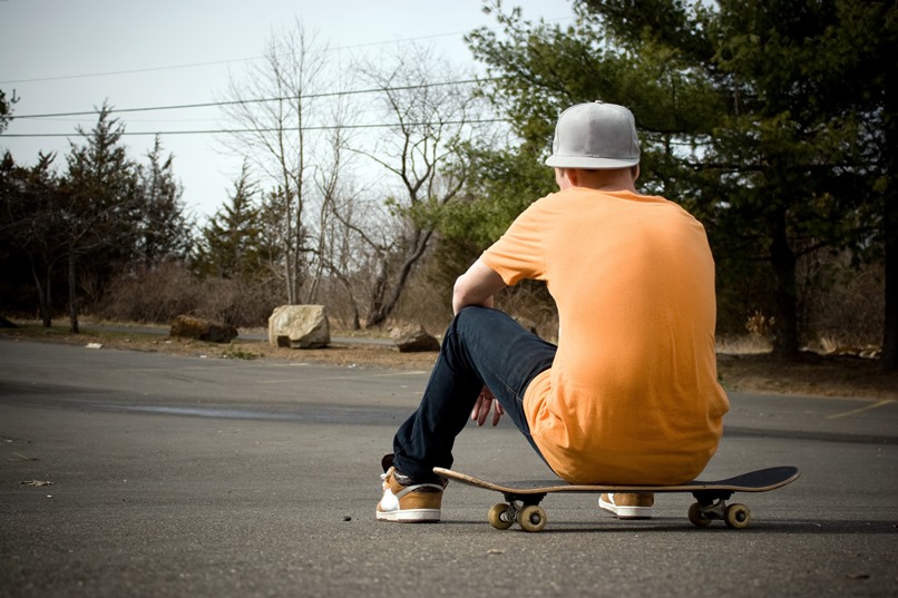 Pojke sitter på skateboard med ryggen mot kameran