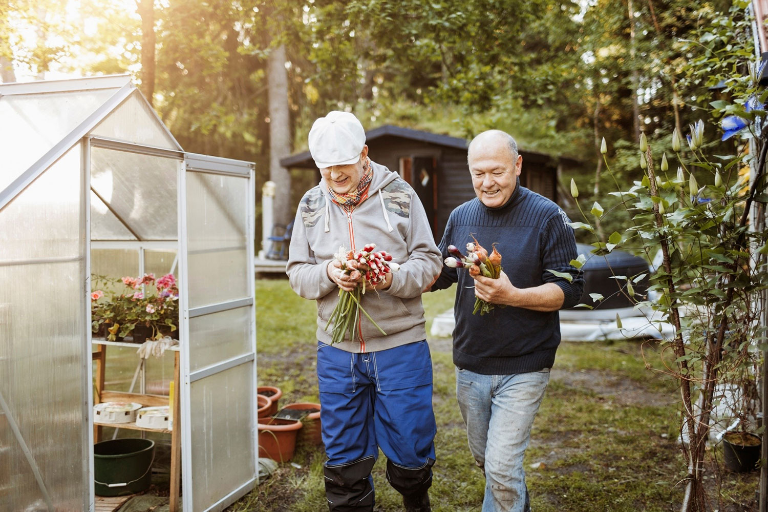En äldre man och en medelålders man med grönsaker i händerna vid ett växthus