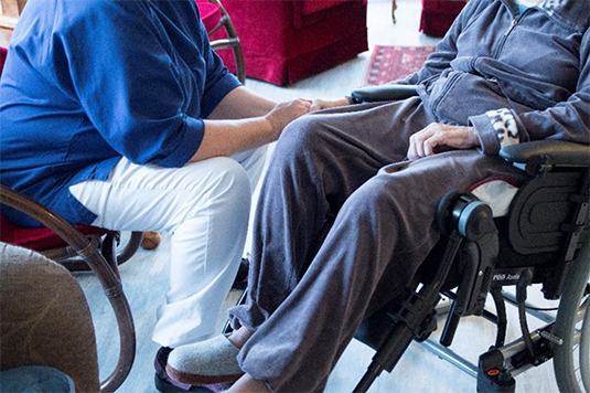 Person som håller en äldre person i rullstol i handen