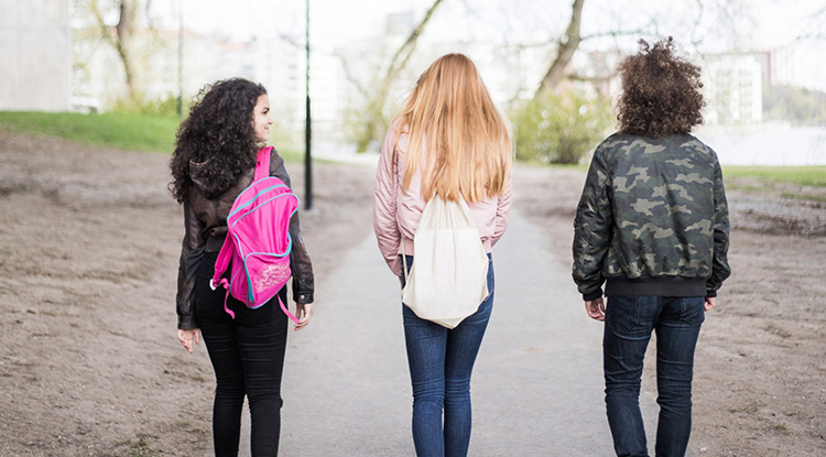 Tre ungdomar med ryggsäckar gåendes bortåt